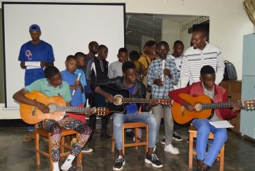 A group of people sitting at a table with a guitar Description automatically generated